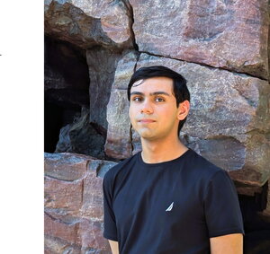 A man in a blue t-shirt standing in front of rocks
