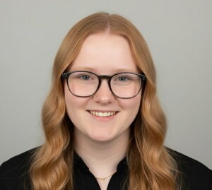 A smiling redhead in glasses and a black shirt