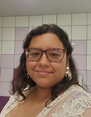 A smiling woman in glasses in front of tiled wall