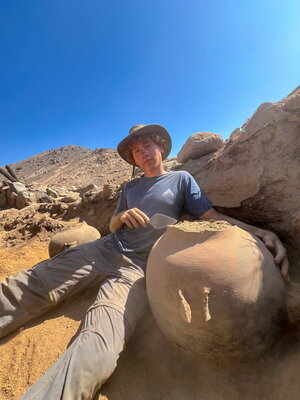 A man in a hat and blue shirt lounging on rocks in the desert
