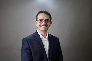 A smiling man in glasses wearing a blue blazer and button up shirt