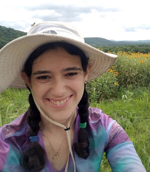 A smiling person in a floppy hat outside