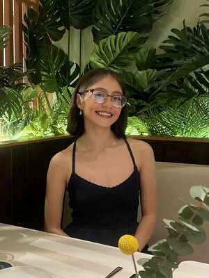 A smiling woman in glasses and a black dress sitting in front of some plants