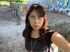 A woman in glasses taking a selfie with a graffitti wall behind her