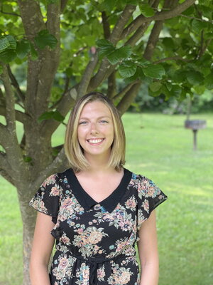 A smiling woman in a flowery dress standing outside in front of a tree