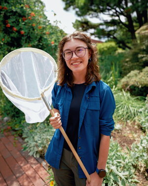 A smiling woman in an open blue button down holding a net and standing outside