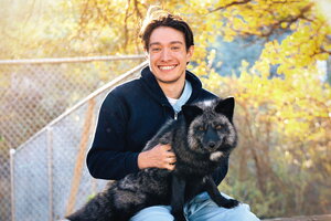 A smiling man in a sweater sitting outside holding a dog