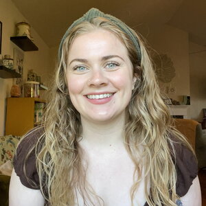 A smiling woman with long hair wearing a brown shirt