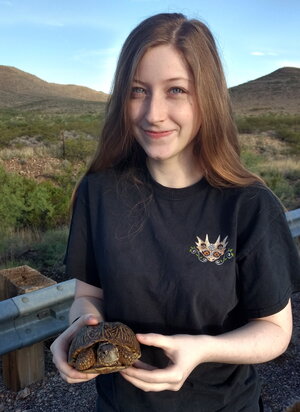 A woman in a black shirt holding a box turtle outside