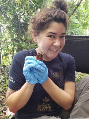 A smiling woman with her hair in a bun wearing blue latex gloves and handling a bird