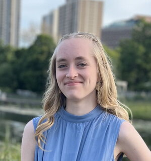 A smiling woman in a blue shirt with tall buildings in the background