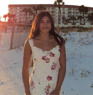 A woman in a flowery dress standing on a beach with a condo in the background