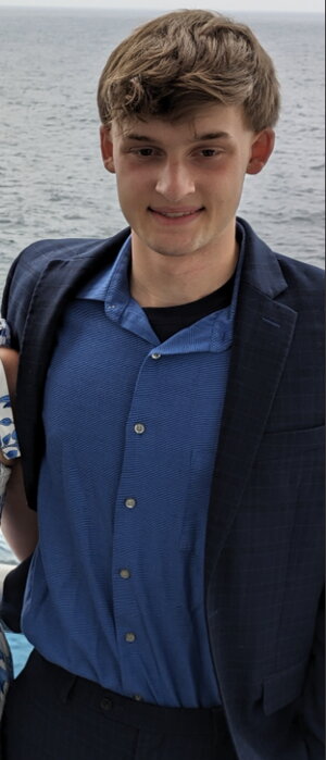 A man in a blue suit jacket and button up shirt standing in front of the ocean