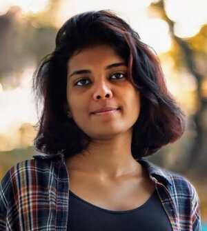 A smiling woman in an open plaid shirt with a blurred natural background