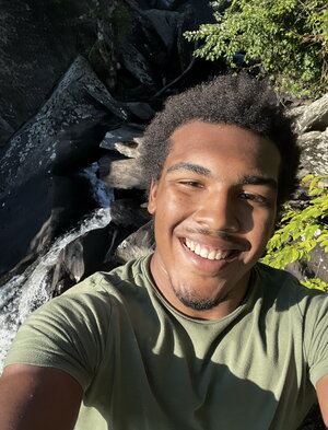 A smiling man in a green shirt taking a selfie with plants in the background