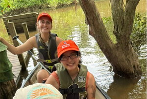 Two smiling women in orange hats smiling in life vests sitting in a boat