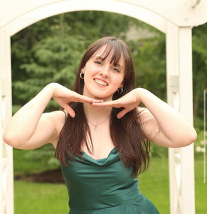 A smiling woman in a green dress with her hands under her head while standing outside