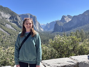 A smiling woman in a green sweater standing outside with mountains behind her
