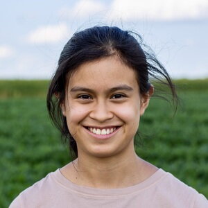 A smiling woman in a pink shirt standing outside by a field