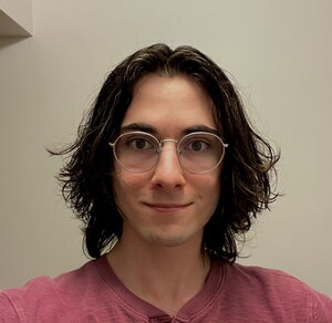 A smiling person with dark hair and round glasses in a red shirt