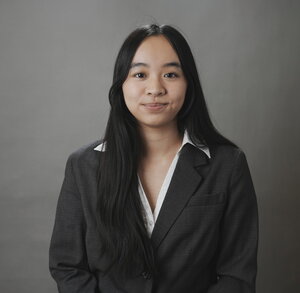 A semi-smiling woman in a grey and white outfit