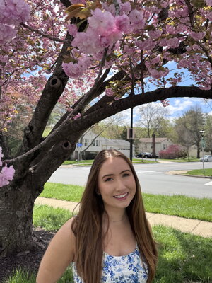 A woman in a flowery dress standing in front of tree with pink flowers
