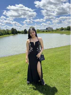 A woman in a black dress smiling in front of a small pond 
