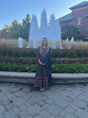 a blonde woman in a dress standing in front of a fountain