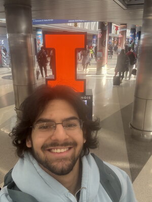A smiling bearded man with longer hair standing in front of the block I