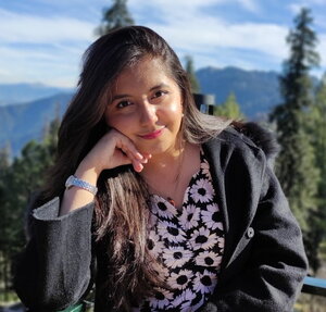 A smiling woman with her head on her hands with trees and mountains in the background