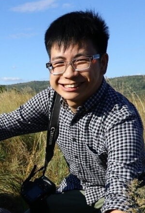A smiling man in a plaid shirt sitting in a field