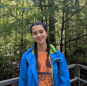 girl in blue jacket, orange shirt, standing in a wooded area