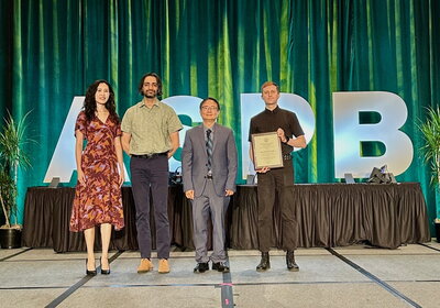 A woman and three men standing on a stage holding an award