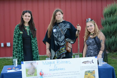 three students wearing cosplay behind a table with a poster in front