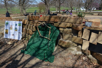 A display set up against stacked rocks with a green tarp and poster board