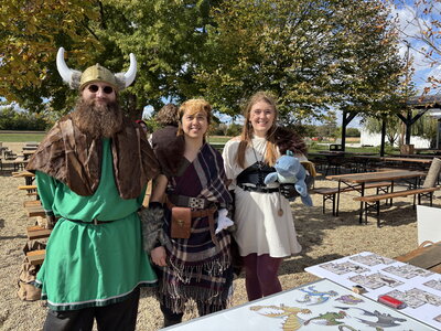 Three people in viking garb smiling in front of a table outside