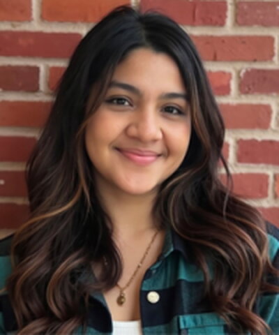 A smiling woman in a green and black flannel standing in front of a brick wall