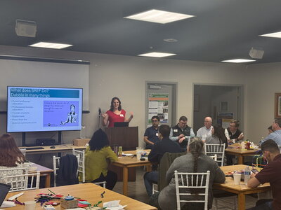 A woman presenting at a podium in a room full of people