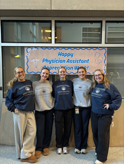 A group women standing and smiling in front of a sign