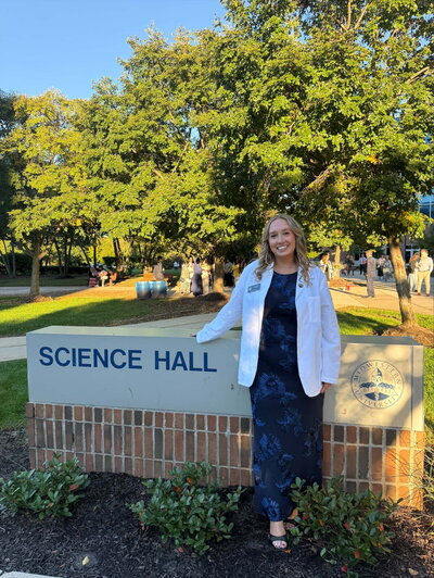 A smiling woman in glasses standing next to a sign outside