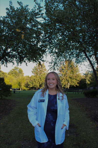 A smiling woman in a lab coat standing outside