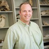 smiling man in front of shelves with animal skulls