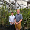 two men standing in front of plants.