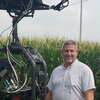 A photo of a man with a machine standing next to a corn field