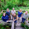 A group of people standing on a wooden platform with woods behind them