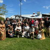 A group of people standing and kneeling in grass wearing fantasy cosplay, with a building behind them