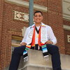 a man in graduation regalia sitting on a stone platform