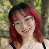 A smiling person with red hair and glasses outside