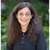 A smiling woman in a blue buttoned shirt standing outside