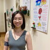 A smiling woman in a tank top standing next to posters hanging on a wall